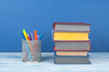 Kitap istifleme. Açık kitap, ahşap masa ve mavi arka plan üzerine ciltli kitaplar. Okula dönelim. Metin için alanı kopyala