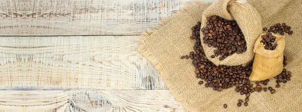Opened burlap bags, a cup of coffee, scattered whole coffee beans on a white background. Banner