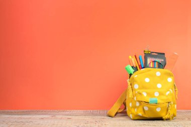 Sırt çantasında farklı renkte kırtasiye malzemeleri var. Turuncu arka plan. Okula geri dön.