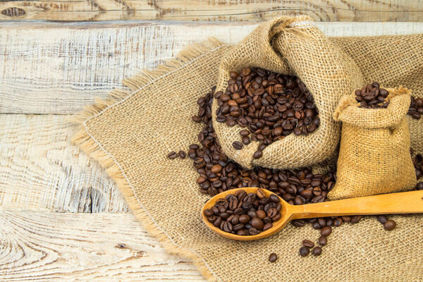 Opened burlap bags, a cup of coffee, scattered whole coffee beans on a white background