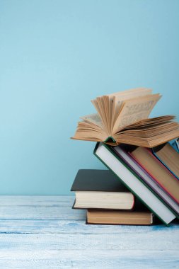 Kitap istifleme. Açık kitap, ahşap masa ve mavi arka plan üzerine ciltli kitaplar. Okula dönelim. Metin için alanı kopyala