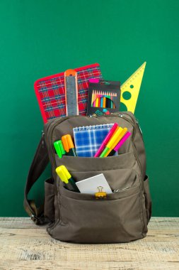 Sırt çantasında farklı renkte kırtasiye malzemeleri var. Yeşil arka plan. Okula geri dön.