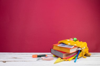 Sırt çantasında farklı renkte kırtasiye malzemeleri var. Burgonya arkaplanı. Okula geri dön.