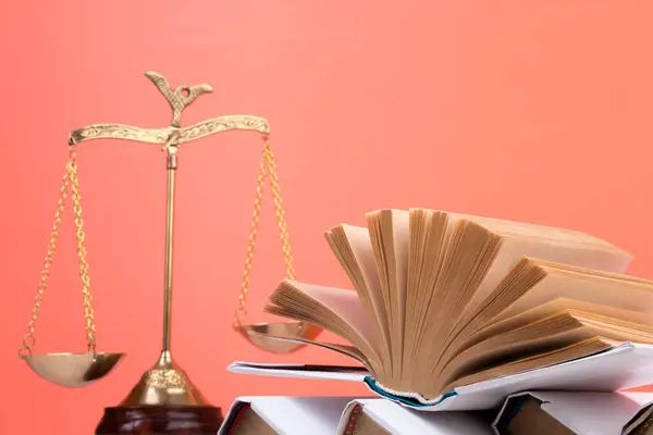 stock image Law concept - Open law book, Judge's gavel, scales, Themis statue on table in a courtroom or law enforcement office. Wooden table, orange background