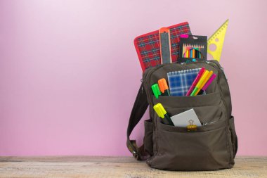 Sırt çantasında farklı renkte kırtasiye malzemeleri var. Pembe arka plan. Okula geri dön.