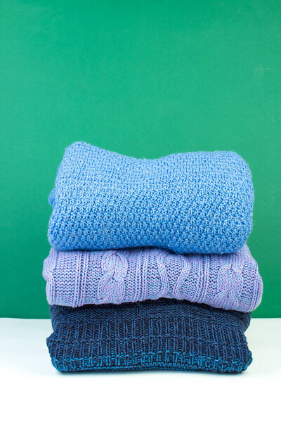 Knitted woolen sweaters. A bunch of knitted winter, autumn clothing on a green background, sweaters, knitwear, space for the text