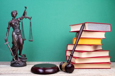 Hukuk konsepti - açık hukuk kitabı, yargıç tokmağı, teraziler, mahkeme salonundaki ya da kolluk kuvvetlerindeki heykel. Tahta masa, yeşil arkaplan.