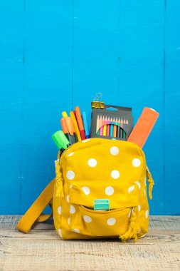 Sırt çantasında farklı renkte kırtasiye malzemeleri var. Mavi arka plan. Okula geri dön.