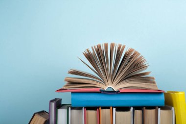 Kitap istifleme. Açık kitap, ahşap masa ve mavi arka plan üzerine ciltli kitaplar. Okula dönelim. Metin için alanı kopyala