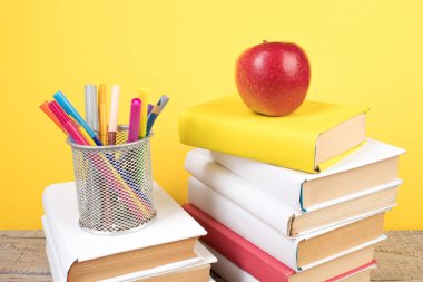 Kitaplar istifleniyor. Tahta masadaki kitaplar ve sarı arka plan. Okula dönelim. Reklam metni için alanı kopyala