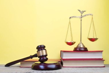 Hukuk konsepti - açık hukuk kitabı, yargıç tokmağı, teraziler, mahkeme salonundaki ya da kolluk kuvvetlerindeki heykel. Tahta masa, sarı arka plan..