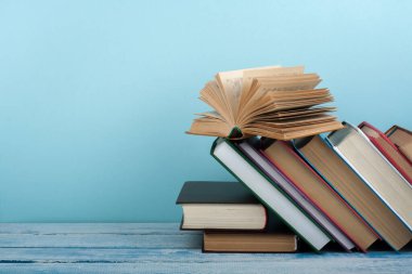 Kitap istifleme. Açık kitap, ahşap masa ve mavi arka plan üzerine ciltli kitaplar. Okula dönelim. Metin için alanı kopyala