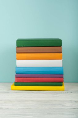 Kitap yığını, ahşap masa ve mavi arka planda ciltli renkli kitaplar. Okula dönelim. Uzayı metin için kopyala. Eğitim kavramı