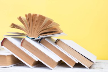 Açık kitaplar, ahşap masada ciltli renkli kitaplar. Sarı arka plan. Okula dönelim. Uzayı metin için kopyala. Eğitim sektörü kavramı