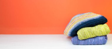 Yünlü yün kazaklar. Kış örgüsü, turuncu arka planda sonbahar kıyafetleri, kazaklar, örgü giysiler, yazı için yer. Pankart