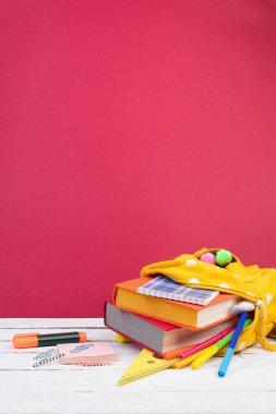 Sırt çantasında farklı renkte kırtasiye malzemeleri var. Burgonya arkaplanı. Okula geri dön.