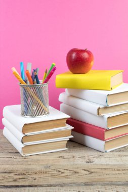Kitaplar istifleniyor. Tahta masadaki kitaplar ve pembe arka plan. Okula dönelim. Reklam metni için alanı kopyala