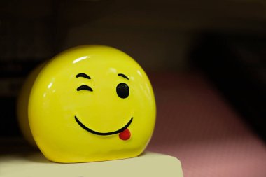 Sarı fotoğraf, parlak güzel emoji, gülüşü ve koyu bir arka planda neşeli bir ifade.