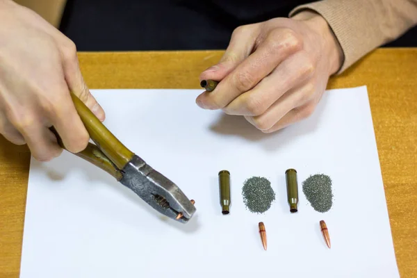 Mens hands with pliers pull out a bullet from a cartridge case.
