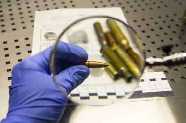 Bir uzmanın lastik eldivenindeki bir el parmak izi kartının arka planında bir mermi tutar..