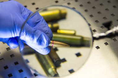 Lastik eldivendeki bir uzmanın eli büyüteçin altında bir mermi tutar..