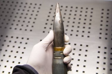 Projectile, cartridge, cartridge case in a mans hand in a rubber glove.