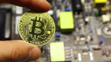 A mans hand holds a bitcoin coin against the background of a microcircuit, board.