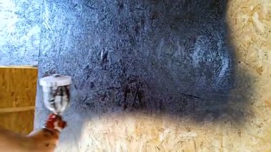 Sprey tabanca kullanan bir adam duvarın yüzeyine eşit miktarda boya dağıtır..