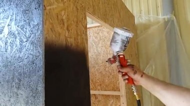 Sprey tabanca kullanan bir adam duvarın yüzeyine eşit miktarda boya dağıtır..