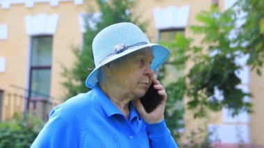 Büyükanne, mavi şapkalı yaşlı bir kadın cep telefonuyla iletişim kuruyor..