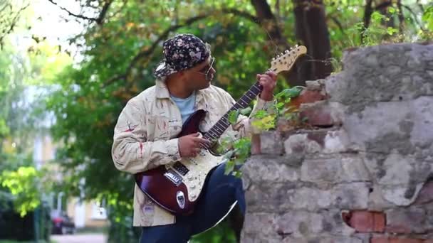 キャップのミュージシャンがアウトドアでエレクトリックギターを演じる — ストック動画