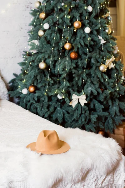 New Years photo zone, New Years interior with a Christmas tree and a bed. Terracotta hat on white bedspread on bed.