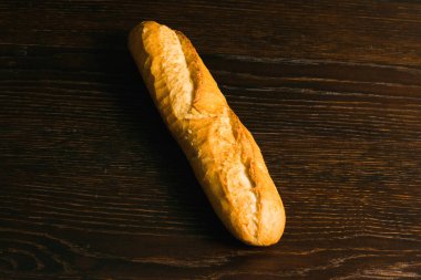 Appetizing french baguette with crust on dark wooden table, background with space for text.