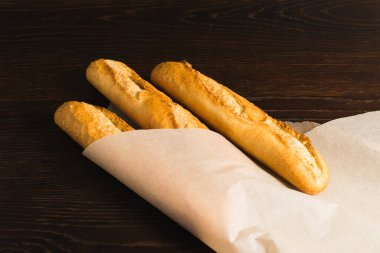 Delicious baguettes from the bakery wrapped in baking paper, on a dark wooden background.
