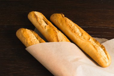 Delicious baguettes from the bakery wrapped in baking paper, on a dark wooden background.