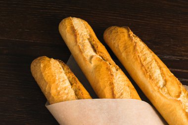 Delicious baguettes from the bakery wrapped in baking paper, on a dark wooden background.