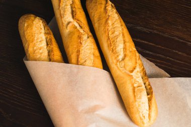 Delicious baguettes from the bakery wrapped in baking paper, on a dark wooden background.