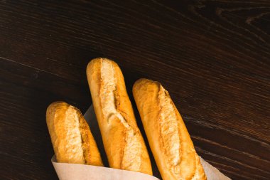 Delicious baguettes from the bakery close-up, wrapped in baking paper, on a dark wooden background with copy space.