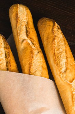 Delicious baguettes from the bakery wrapped in baking paper, on a dark wooden background.