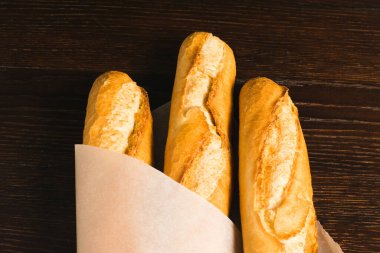 Delicious baguettes from the bakery close-up, wrapped in baking paper, on a dark wooden background with copy space.