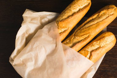 Delicious baguettes from the bakery wrapped in baking paper, on a dark wooden background.