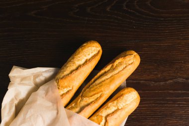 Delicious baguettes from the bakery wrapped in baking paper, on a dark wooden background.