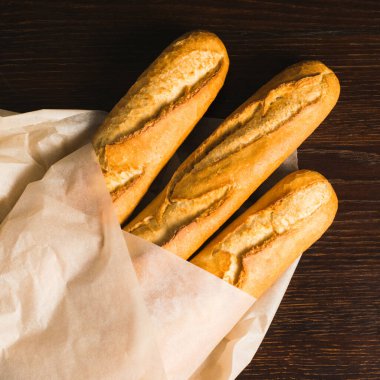 Delicious baguettes from the bakery wrapped in baking paper, on a dark wooden background.