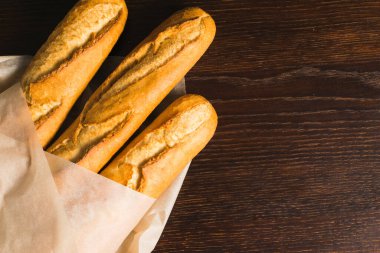 Delicious baguettes from the bakery close-up, wrapped in baking paper, on a dark wooden background with copy space.