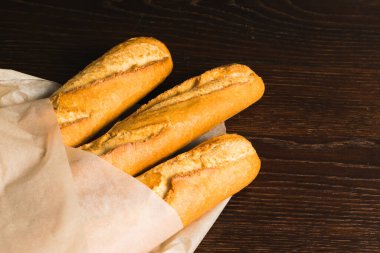 Delicious baguettes from the bakery close-up, wrapped in baking paper, on a dark wooden background with copy space.