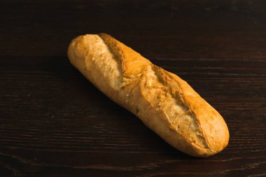 Appetizing french baguette with crust on dark wooden table, background with space for text.