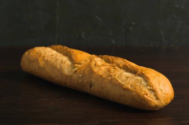 Appetizing french baguette with crust on dark wooden table, background with space for text.