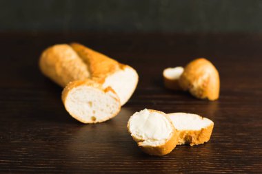 Slice of baguette with butter on wooden background. Sliced French baguette on a dark wooden table.