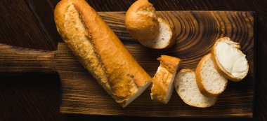 Appetizing baguette with butter on a wooden cutting board, flatlay.