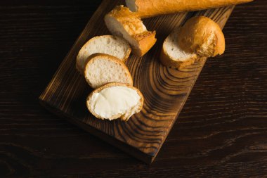 Delicious baguette with butter on a wooden cutting board close-up, flatlay.